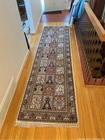 Full length view of the long runner rug laid out on wood floor showing the overall pattern and fringes at the bottom end.