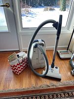 Front view showing canister body, hose, wand, floor head and accessory bag