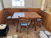 Dining table with five chairs, arranged around a corner near windows with wood paneling on walls.