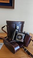 Vintage Welta folding camera partially out of original brown leather carrying case on a table.