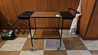 Front side view of wheeled warming/serving cart showing metal frame, wood panel shelves, caster wheels, and handle