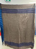 Full front view of the brown blanket with blue stripes along the edges, showing size and color pattern.