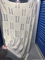 Full view of the cream crochet blanket held up to show overall design and scale.