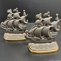 Front view of both bronze ship bookends showing shape, detail and condition.