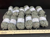 Multiple balls of 1-ounce green acrylic blend yarn with white labels and some specks of other colors in the yarn strand, laid out with a ruler.