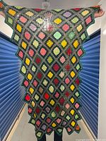 Full view of the crochet throw blanket held up, showing colorful flower motifs in diamond grid pattern with scalloped edging