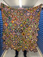 Man holding large crochet blanket showing full colorful square pattern with diagonal arrangement and scalloped edge.