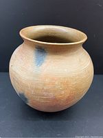 Photo showing side view of the large terracotta cooking vessel urn with its rounded bulbous shape and natural clay color with black smudges.