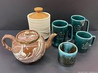 Photo showing the brown and white marble-effect ceramic teapot with lid, beige lidded canister, and four blue-green glazed mugs with Centennial star and 1967 date.