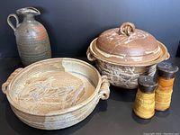 Front view of all five pottery items comprising the lot: two casserole dishes, jug, and salt and pepper shakers, showing the art glazing, handles, and textures.