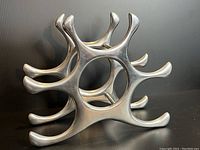 Front angle of stainless steel modernist wine bottle holder showing six protruding arms for holding bottles.