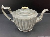 Front and side view of pewter teapot showing etched ribbed design, spout and side handle.