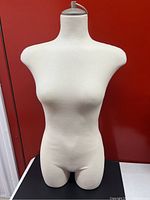 Front view of the plush female dress form on a black and white table with a red background.