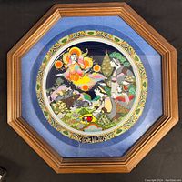 Framed octagonal wooden frame with glass covering a colorful decorative porcelain plate portraying a Christmas carol scene with angelic figure and woodland characters