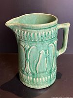 Side front view of the Roseville Robinson yellow-green pitcher showing the handle, spout and embossed decorative pattern.