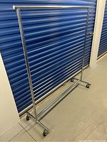 Full view of the stainless steel garment rack showing its structure and wheels.