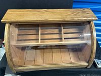 Front view of vintage wood tabletop display case with curved clear plexiglass, wooden shelf with dividers inside, showing wood grain and lock.