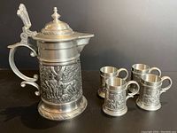 Full view of the pewter pitcher with hinged lid and four matching shot glasses decorated with relief scenes