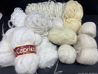 Overview of white and cream yarn balls and skeins including Caprico branded bulky yarn and various mohair blend yarns.