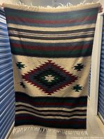 Full view of woven Navajo Aztec tapestry blanket held up showing full front with geometric pattern and fringe edges