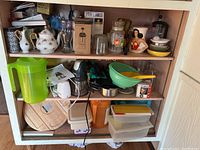 Three shelves filled with various kitchen and household items such as pitchers, mixer, teapot, glass jars, containers, and decor items.