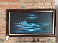 Framed ocean wave painting hanging on a stone wall, showing the full artwork and frame.