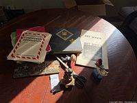 Boy Scouts related items on a wooden table including an album/binder, confidential information folder, art songs booklets, scissors, a figurine, and tape dispenser.