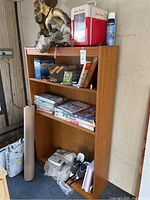 Photo showing wooden cabinet with board games, books, plastic bag with mixed items, shoes, packing paper roll on the side