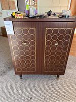 Closed view of small side table cabinet with dark wood finish and gold geometric circle patterns on doors.