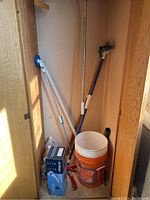Photo of storage closet showing cleaning tools and supplies including two mops, two orange buckets, gloves, cleaning rags, and spray bottle