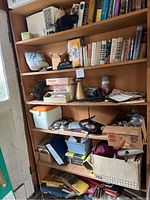 Wooden shelves with multiple items including books, cooler, containers, papers, headset, small cardboard boxes, and miscellaneous household and office items.