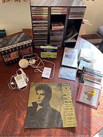 Full lot overview showing signed David Copperfield program, media storage rack filled with CDs, assorted CDs and DVDs, white iPod, Verbatim CD-R spindle, and VHS tapes in storage box.