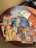 Several MAD magazines spread out on a round wooden table showing a variety of covers and issues