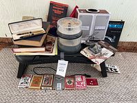 Overview of entire lot showing all items displayed on a bench including books, pens, matchbooks, coffee grinder, and other small items