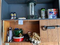 Shelf with assorted household items including electric lantern, cleaning products, gloves, vintage tin and green glass jar