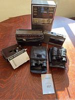 Lot of radios, binoculars, camera displayed on wooden surface