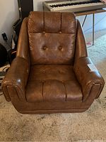 Front view of brown rocking and swivel chair showing cushioned seat, button tufted backrest, and armrests.