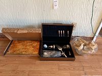Silver plate utensils displayed in wooden black-lined case, glass bowls with packing paper adjacent