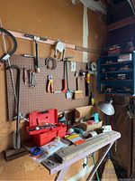 Full view of various tools hung on a pegboard above a workbench and some items on the bench showing tool assortment and display.