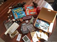 Wide shot of all items in the bundle on a wooden table including Shrinky Dinks kits, animal figurines, electronic game, and other assorted toys and cards.
