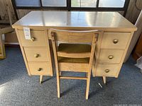 Full view of vintage wooden desk with six drawers and round brass knobs, paired with a wooden chair with upholstered seat.