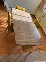 Top down angle showing full rectangular table with three matching yellow-green upholstered chairs around it, placed on wood floor with carpet edge visible