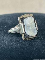 Angled three-quarter view showing carved Greek figure cameo and square stepped gold setting