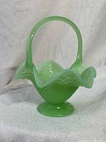 Front angled view of the green jadeite Fenton fruit bowl basket showing textured diamond pattern, scalloped rim, and handle.