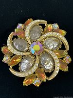 Top-down photo of vintage gold brooch showing all stones and swirl design