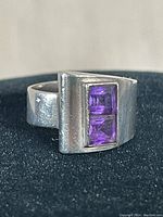Close-up of sterling silver amethyst ring angled to show the two square amethyst stones recessed into a solid silver band with a brushed finish.