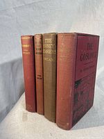 Four Upton Sinclair books standing upright: Mammonart (red spine), Samuel The Seeker (lighter red spine), The Money Changers (brown spine), The Goslings (red cover with black title and illustration)