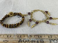 Two vintage bracelets: one tiger eye beaded with gold clasp, one gold-tone chain with purple stones and spike charms