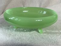 Side view of the green jadeite candy bowl showing its translucent green glass and three legs.