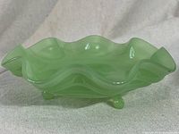 Side view of the green jadeite fruit bowl showing rolled and ribbed edge and three small ball feet.